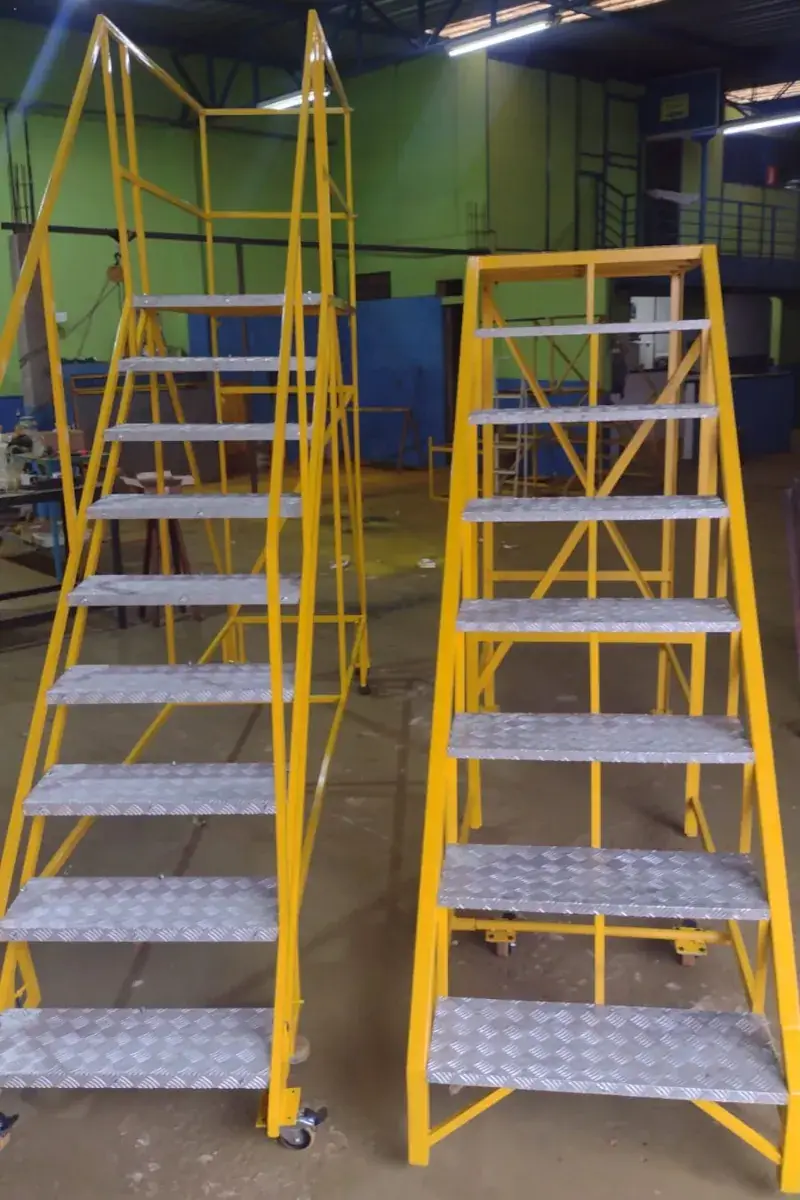 Duas escadas de plataforma amarelas com degraus de chapa xadrez na oficina da Aero Metal